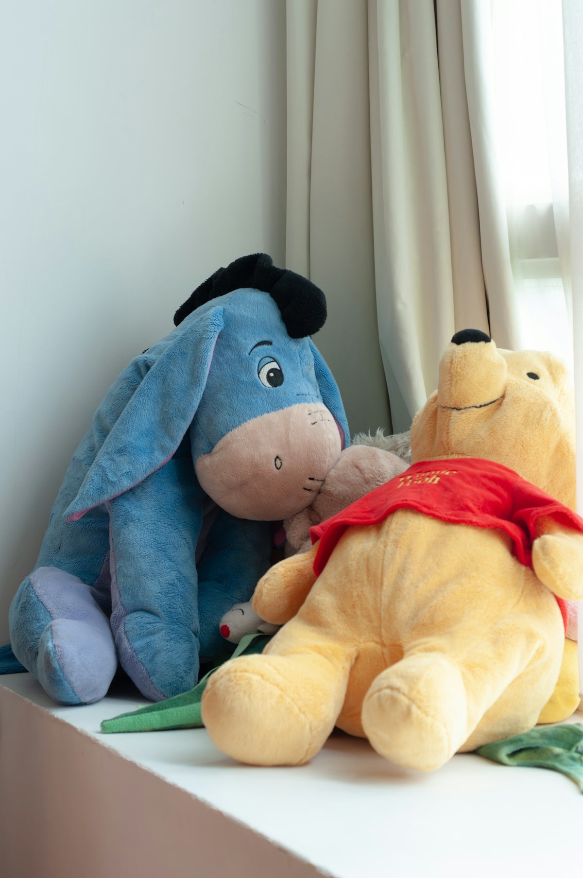Winnie the pooh and eeyore plush toys on a windowsill.